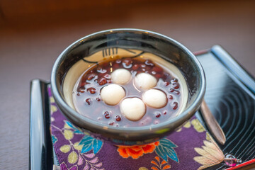 Shirakawa village, Gifu, Japan. A bowl of sweet red bean soup topped with mochi balls, served on a decorative cloth, showcasing traditional Asian dessert culture.
