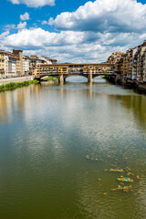 Obraz premium Ponte vecchio over arno river, scenic view of the historic ponte vecchio bridge over the calm waters of the arno river, with surrounding architecture and a cloudy sky in florence, italy.