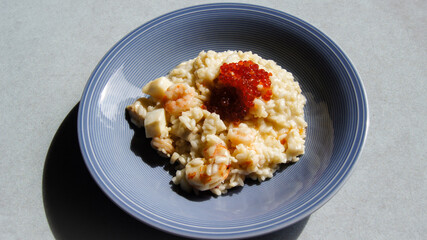 Risotto with shrimps and red caviar and parmesan cheese, Italian risotto with seafood cocktail, seasonal products, Italian fish dishes, on a blue plate, gray background, Italy