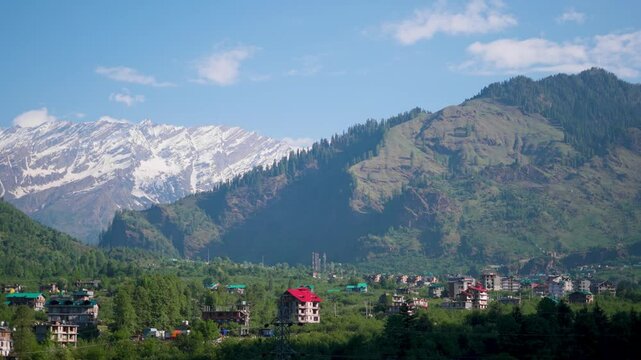 4K Landscape shot of houses and buildings with snowy Himalayan mountain peaks in the background as seen from Manali in Himachal Pradesh, India during the winter season. Manali town during winter.