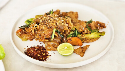 Pad See Ew: A vibrant plate of Pad See Ew, a popular Thai dish featuring stir-fried wide rice noodles, pork, vegetables, and a flavorful sauce. The dish is garnished with fresh lime and chili flakes.