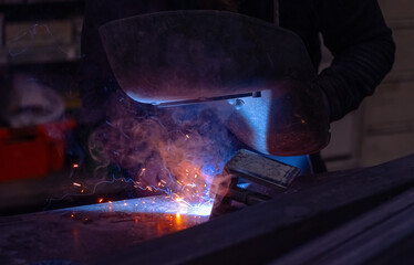 A welder skillfully fabricates metal in a workshop, sparks flying in the dimly lit environment during evening hours
