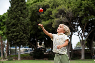 Blonde Toddler Tossing an Apple Playfully in a Lush Green Park
