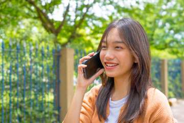 Asian young woman talking on cellphone smiling laughing while walking outdoors in city. 