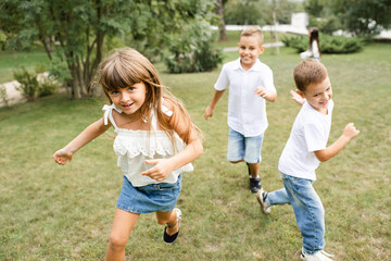 Cute stylish group of children 5 - 6 year old wearing denim clothes running on green grass lawn in park. Happiness. Childhood.