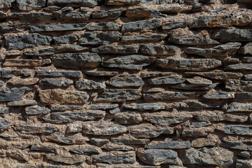 Old ruined masonry made of gray natural stone of different sizes and shapes. Background for design.