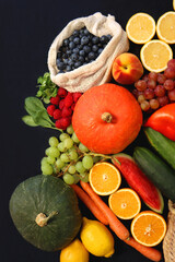 Round straw bag and various seasonal fruits and vegetables on dark background. Summer and fall produce. Top view.