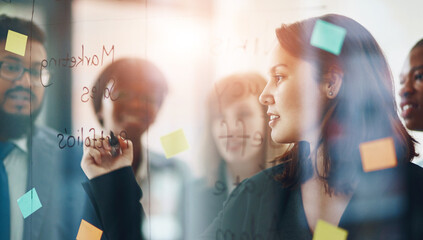 Business people, glass wall and woman writing, brainstorming and strategy in office. Sticky notes, planning and group of employees working on ideas, schedule and collaboration for teamwork at work.