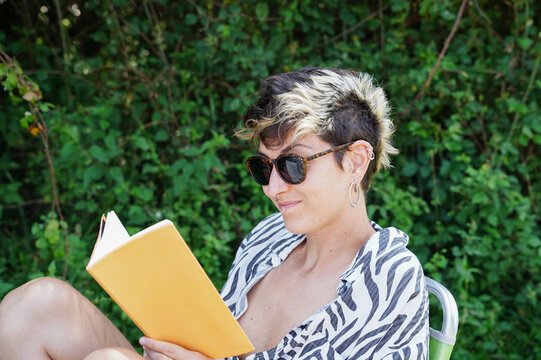 Non-binary person relaxingly reading a book outdoors