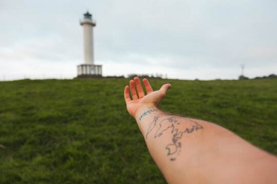Hand reaching toward a lighthouse in Asturias, Spain
