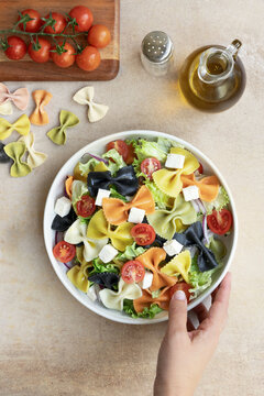 Top view of a person holding colorful farfalle pasta salad with vegetables on a bowl