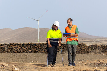 Two workers inspecting wind farm, one using crutches