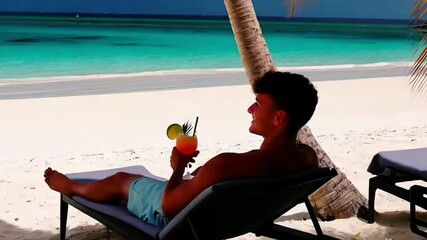 Video footage - relaxing on a sun lounger, a young man sips a colorful tropical cocktail, enjoying the sunny beach and ocean view.