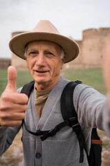 Retired man tourist traveler influencer taking selfie photo on mobile phone camera in ancient fortress traveling vlog