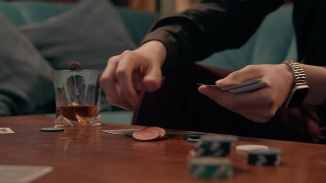 Close up unrecognizable Caucasian male card dealer man guy croupier shuffles deals playing cards poker chips gaming casino gambling play blackjack drinking alcohol whiskey smoking cigar at home room
