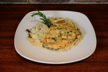 Closeup of a chicken breast served with rice and pepper sauce on a white plate on a wooden table