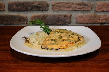 chicken breast served with rice and pepper sauce on a white plate on a wooden table