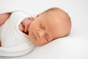 a newborn baby is lying in a diaper on a bed on a white isolated background, a place for text, a small baby boy is sleeping sweetly, a close-up portrait