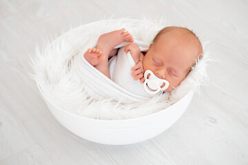 a newborn baby lies in a diaper on the bed and sucks a pacifier on a white isolated background, a place for text, a small baby boy is sleeping sweetly, a close-up portrait