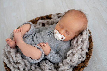 a newborn baby with a pacifier sleeps in a gray bodysuit, a place for text, a small baby boy sleeps...