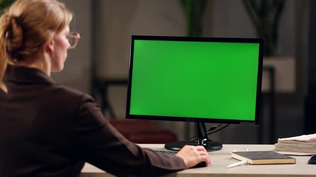 Young Woman Working In Office On Desktop Computer with Green Screen Mock Up Display. Over the Shoulder- Close-up of Monitor With Green Screen Chromakey
