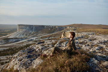 Naklejka premium Scenic view of woman sitting on cliff edge overlooking valley and mountains in travel adventure landscape concept