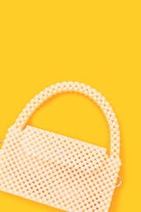 Handicraft bag made from pearl imitation beads on a yellow background with copy space.