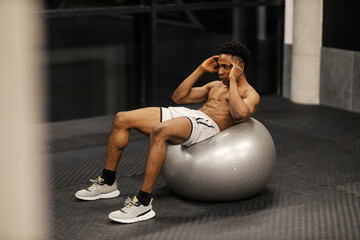 Naklejka premium Strong muscular shirtless diverse sportsman doing crunches on fitness ball at gym.
