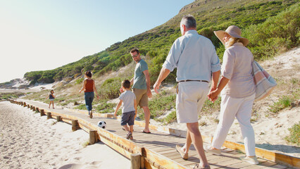 Multi-Generation Family On Summer Vacation Walking Along Wooden Boardwalk On Way To Beach