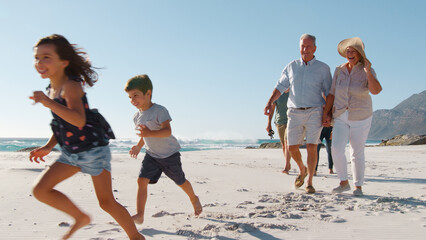 Multi Generation Family Meeting As They Walk Along Sandy Beach On Summer Vacation