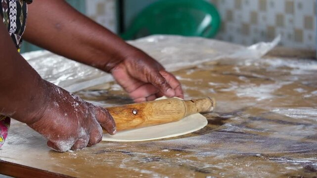 Hands rolling dough with a wooden pin, preparing Kenyan chapati on a floured surface