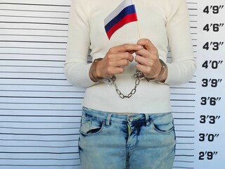 A handcuffed woman holds a small Russian flag at a police station