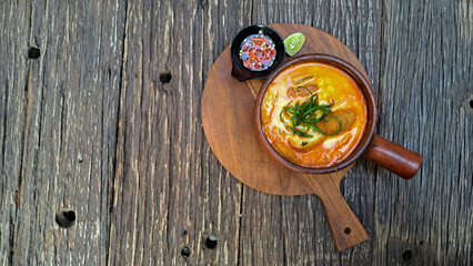 Laksa, spicy noodles served in a pot with lime wedges and sambal. Isolated wooden background.