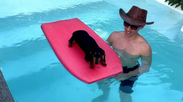 homem na piscina com cachorro salsicha em prancha de surfe
