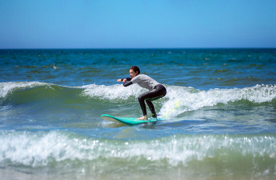 Teenage girl learning to surf on foam in the ocean. First surfing lesson. Amateur surfer. Surfing training. Photo for surfing school advertising on social media.
