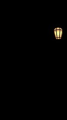 A single streetlight glows against a pitch-black sky, casting a warm, inviting light into the darkness