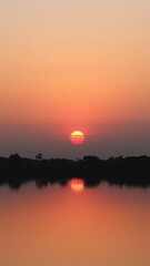 Obraz premium Tranquil sunset over a calm lake, with vibrant orange and pink hues reflecting on the water