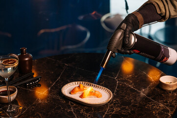 Close-up of a chef carefully searing a nigiri sushi with a culinary blowtorch.