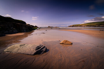 A rock rests on the sandy beach near a glistening body of water