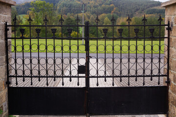 Close huge cemetery gate with outlook outside into the village street and hill and forest, conceptual photo