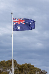 Australia national flag flying on pole against blue sky with cloud background