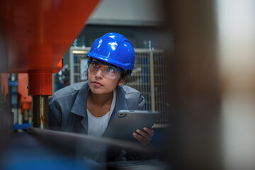 Indian woman engineer with a blue helmet holding a tablet, doing factory working machine...