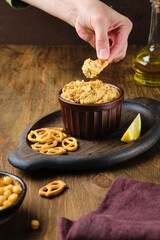 Hummus with sweet potato in a brown ceramic bowl on a brown wooden background. Served with crackers. Chickpea recipes.