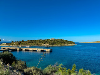 Obraz premium Scenic view of Porto Palermo Quay near Himare, Albania. Idyllic coastline along the Albanian Riviera. Tropical bay in Ionian Mediterranean sea. Ali Pasha castle on small peninsula with clear blue sky