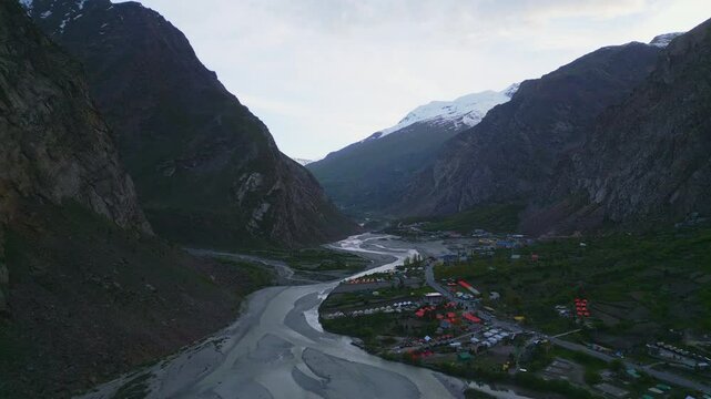 A stunning aerial view of Jispa, Himachal Pradesh, showcasing a serene valley with a winding river, towering mountains, and vibrant campsites nestled in nature.