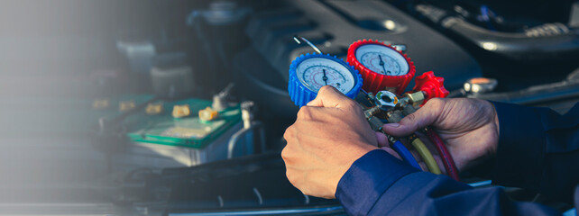 Auto mechanic's hand uses a meter to check for problems with the car's air conditioning system and repairs and refills the air conditioner.