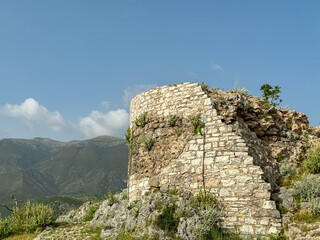 Obraz premium Ruins of an ancient stone building in Himare Castle, Vlore, Albania. Meadow of wildflowers blooming with scenic view of Ceraunian mountain range. Partially collapsed walls of historical site. Discover