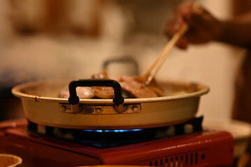 A close-up shot of a sizzling Moo Kata grill, with meats cooking on top and broth simmering below,...