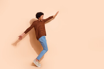 Happy young african american man in casual sweater and jeans posing joyfully on a beige background, expressing cheerfulness and energy.