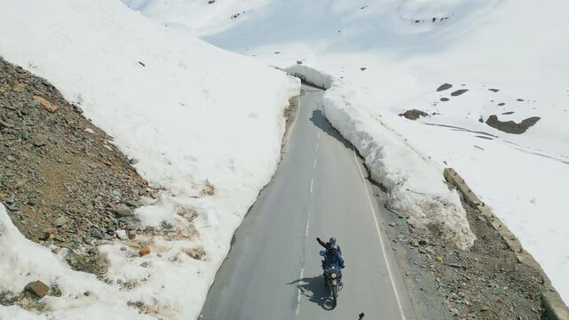 Aerial view of motorcyclists riding through snow-covered Zing Zing Bar in Leh-Ladakh, with towering snow walls, rugged terrain, and winding roads.